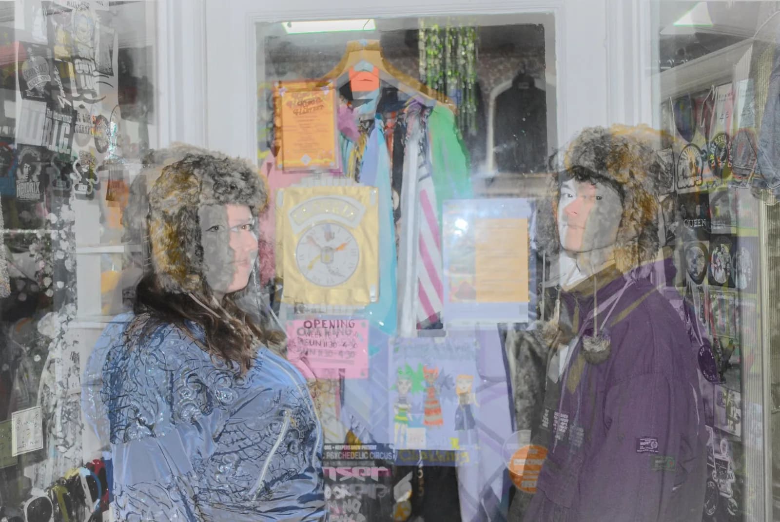 Two people wearing fur hats and winter coats stand in front of a shop window displaying clothing and signs.